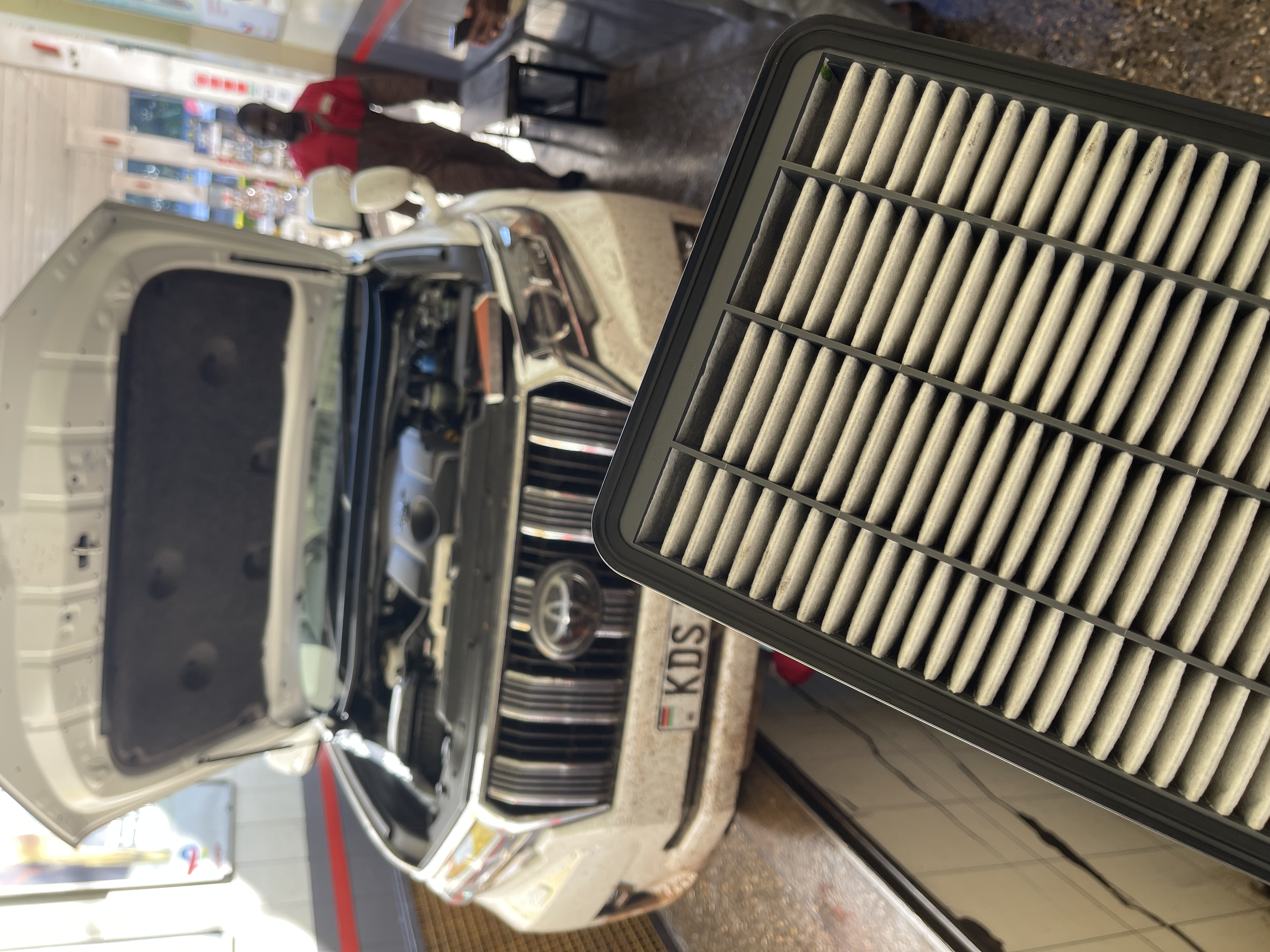 Toyota Land Cruiser Prado with its bonnet open at a service bay and an air filter in the foreground